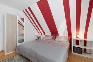 A bedroom with a bed, bedside tables, a wardrobe, and a red and white striped wall.