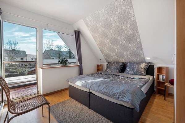 A bedroom with a large bed, a chair, a window with curtains, and a patterned wall.
