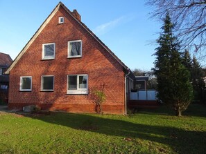 A red brick house with a gabled roof, multiple windows, and a small tree in the yard.
