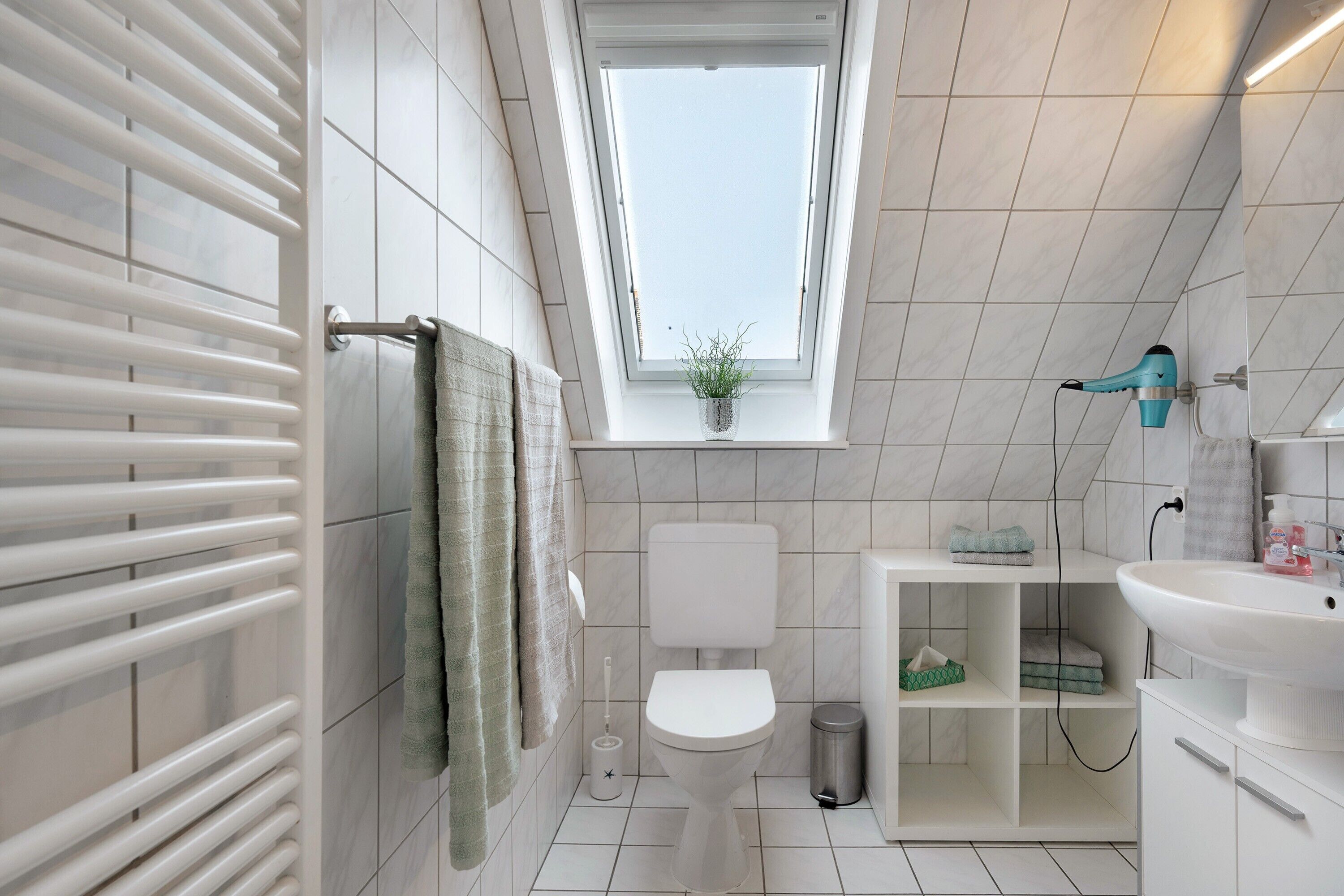 Une salle de bain moderne avec un puits de lumière, des toilettes, un lavabo et un porte-serviettes.