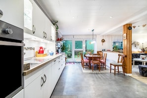 Uma cozinha moderna com armários brancos, uma área de refeições com cadeiras de madeira e vista para um jardim através de portas de vidro.