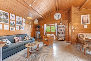 A wooden interior with a sofa, a wicker chair, a table, a bookshelf, and framed pictures on the walls. - Holiday Home 'Moi Holzhaisel' with Private Terrace, Private Garden and Wi-Fi (Elmstein)