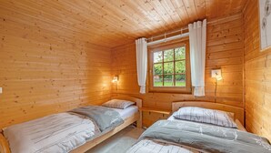 Une cabine équipée de deux lits en bois, d’une fenêtre avec des rideaux et d’un luminaire fixé au mur.