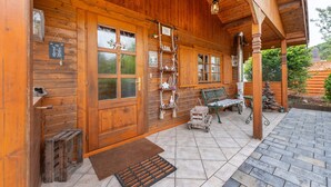 Une cabane en bois avec une véranda, un banc, une échelle et un petit chariot.