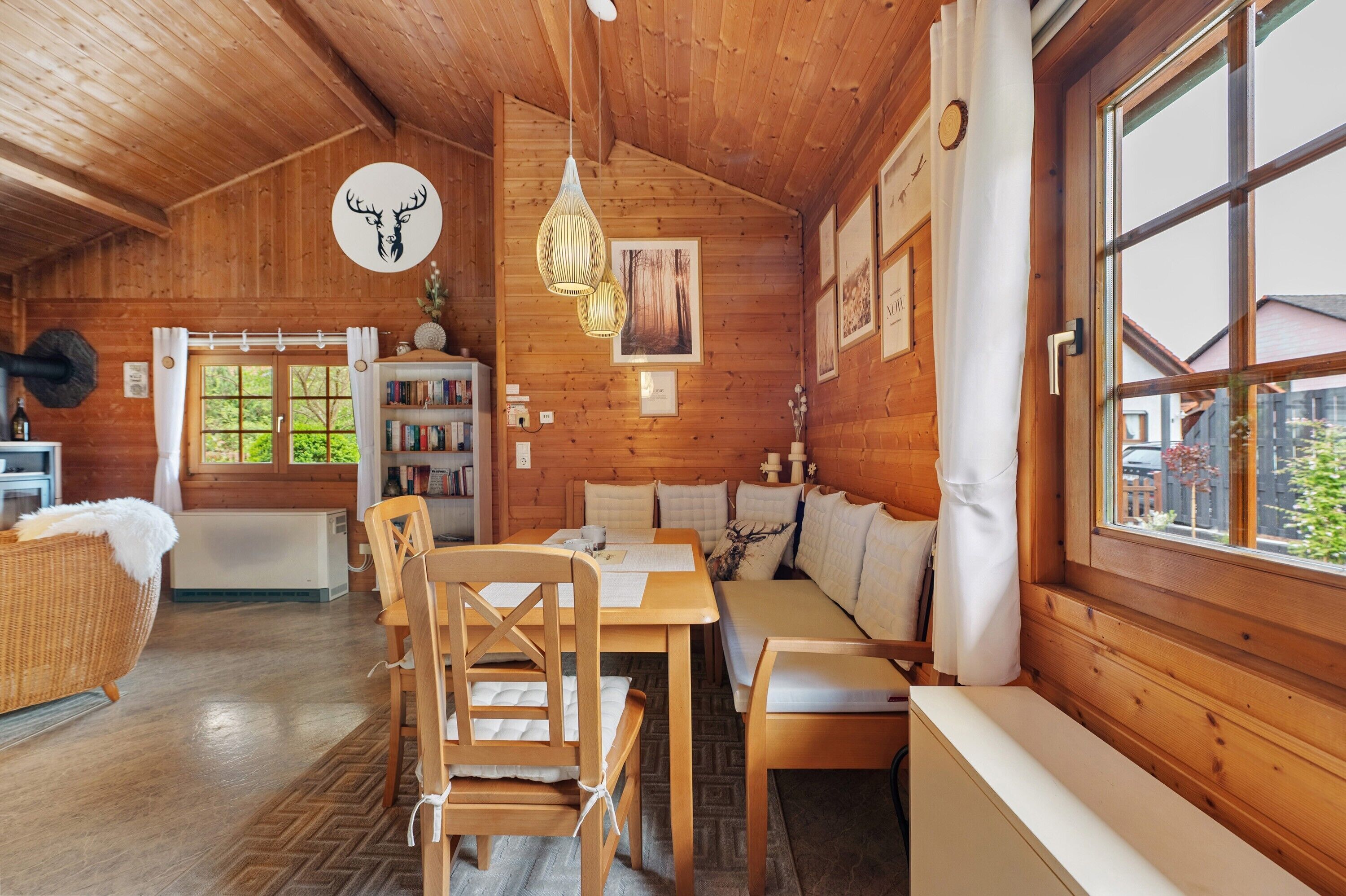 A cozy cabin interior with wooden walls, a dining area, a sofa, and a window with a view.