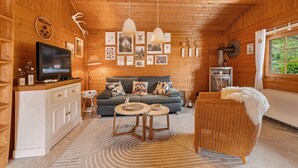 L’intérieur d’un chalet en bois est aménagé avec un canapé, deux tables d’appoint, un téléviseur et des tableaux encadrés accrochés aux murs.