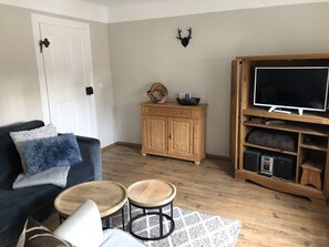 A living room with a dark blue sofa, two wooden side tables, a wooden cabinet, a mounted television, and a wall-mounted deer head decoration. - Holiday Home 'An Der Truse' with Shared Terrace, Private Garden and Wi-Fi (Brotterode-Trusetal)