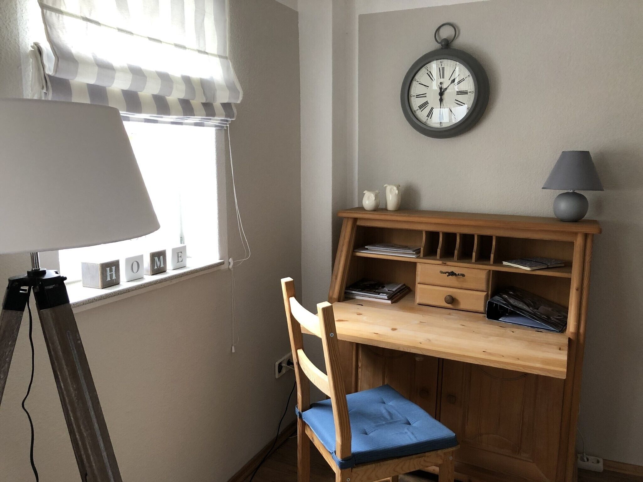 Um quarto com uma escrivaninha de madeira, uma cadeira, um abajur e um relógio de parede.