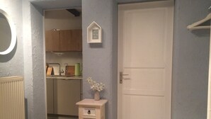 Un pasillo con una puerta blanca, una mesa pequeña con un florero y una zona de cocina al fondo.