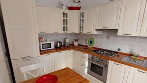 Una cocina compacta con armarios blancos, una encimera de madera, un tazón rojo sobre la mesa y una estufa a gas.