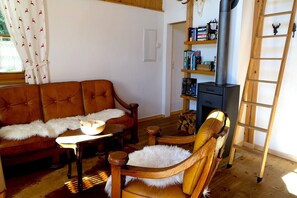Een gezellige woonkamer met een bruine bank, een houten stoel, een klein tafeltje, een boekenkast en een open haard.
