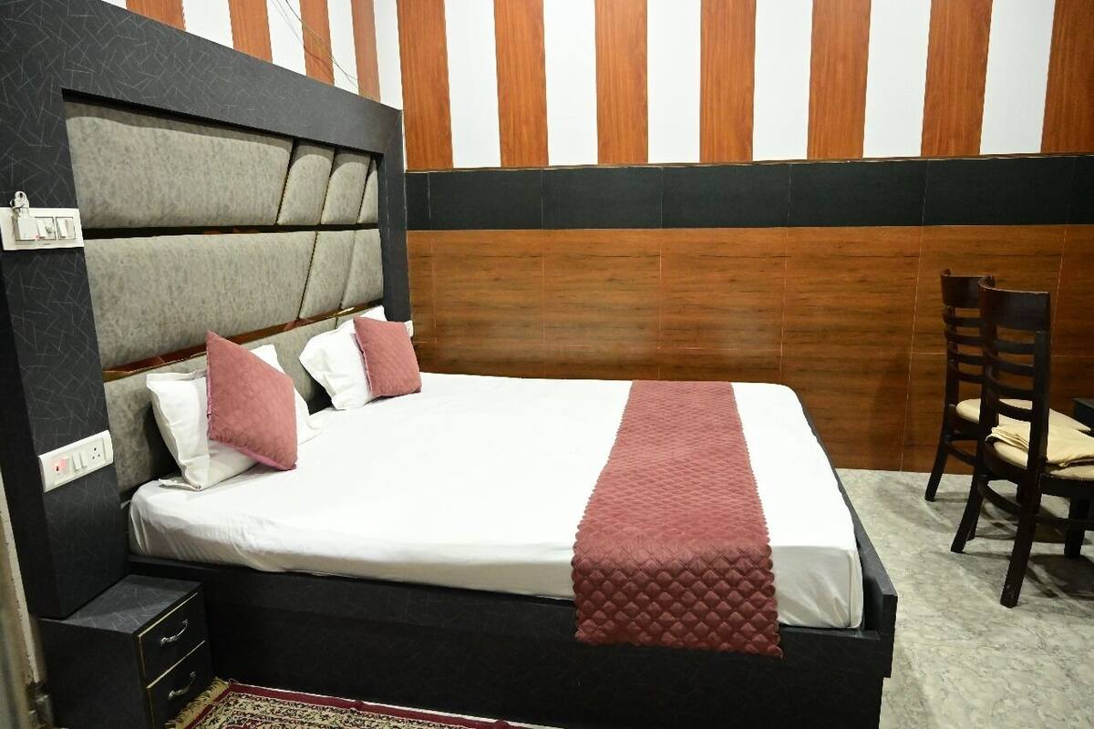 A neatly made bed with a headboard, a bedside table with drawers, a chair, and a striped wall in the background.
