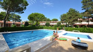 A swimming pool area with clear blue water, surrounded by greenery and buildings. - Stylish home with pool and solarium (Bibione)