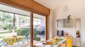 A dining area with a table set for breakfast, a television, and a small cabinet with a plant. - Stylish home with pool and solarium (Bibione)