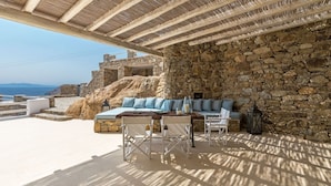 A stone-walled outdoor seating area with a table and chairs, overlooking a coastal landscape. - Villa in Kalafati with 8 bedrooms sleeps 16 (Kalafati)