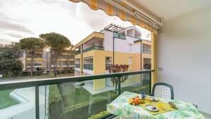A balcony with a table set for breakfast, overlooking a residential building and a green area.