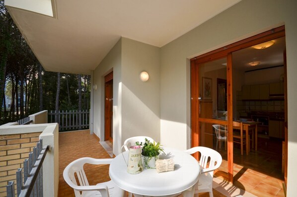 A balcony with a table and chairs, a potted plant, and a bottle of wine.