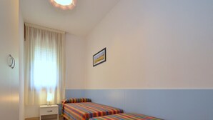 Una habitación pequeña y limpia con dos camas individuales, una mesita de noche, una lámpara y una ventana con cortinas.