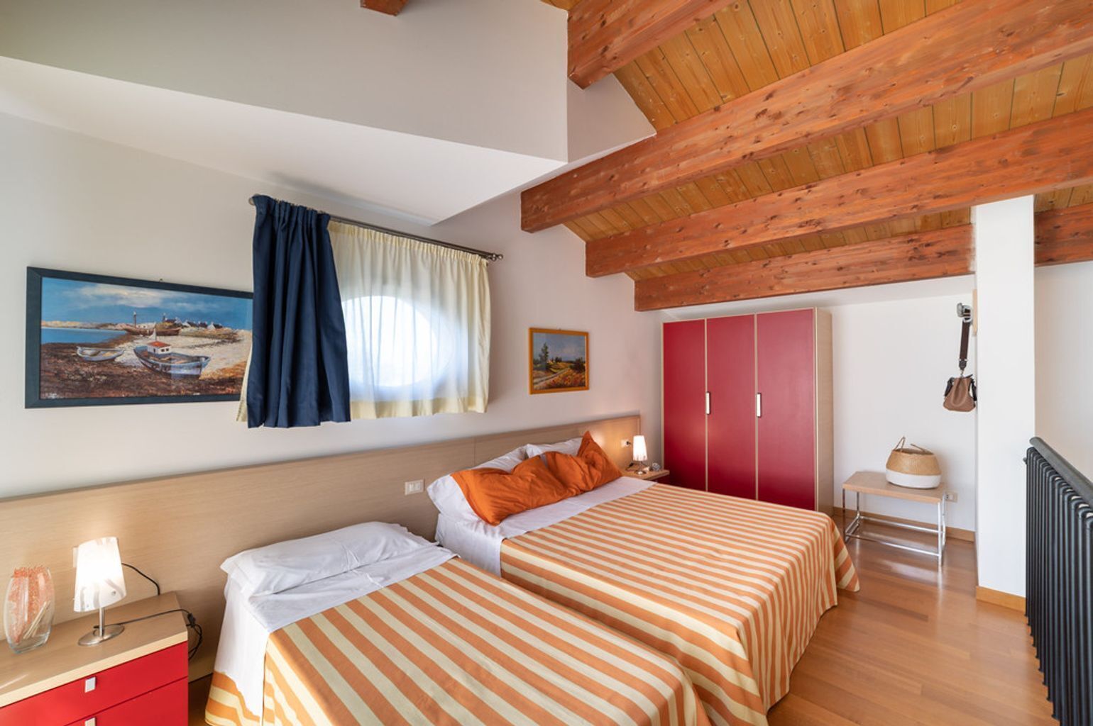 Ein Schlafzimmer mit zwei Betten, einem roten Kleiderschrank, einem kleinen Tisch mit Lampe und einem Bild an der Wand.