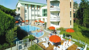 Un complex turístic amb una piscina gran, nombroses parasols i un pont de fusta amb gandules.