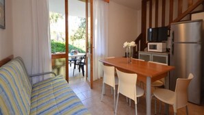 Un salon chaleureux avec un canapé à rayures, une table à manger en bois avec des chaises, une cuisine équipée d’un réfrigérateur et d’un four à micro-ondes, et une porte-fenêtre coulissante donnant sur une terrasse extérieure.