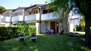 Un immeuble de deux étages doté d’un balcon, d’un petit jardin avec des chaises et d’un arbre.