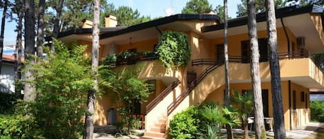 A two-story building with a staircase leading to the upper floor, surrounded by trees and greenery.