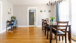 Zona pranzo con tavolo e sedie in legno, un lampadario e vista sulla cucina tramite un'apertura.