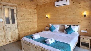 A wooden cabin room with a bed, two wall-mounted lights, an air conditioner, and a small bedside table. - Sand Tent Beach Resort Patnem (Canacona)