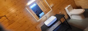 Ein Badezimmer mit Holzwandverkleidung, einem weißen Waschbecken, einem Spiegel und einer Toilette.
