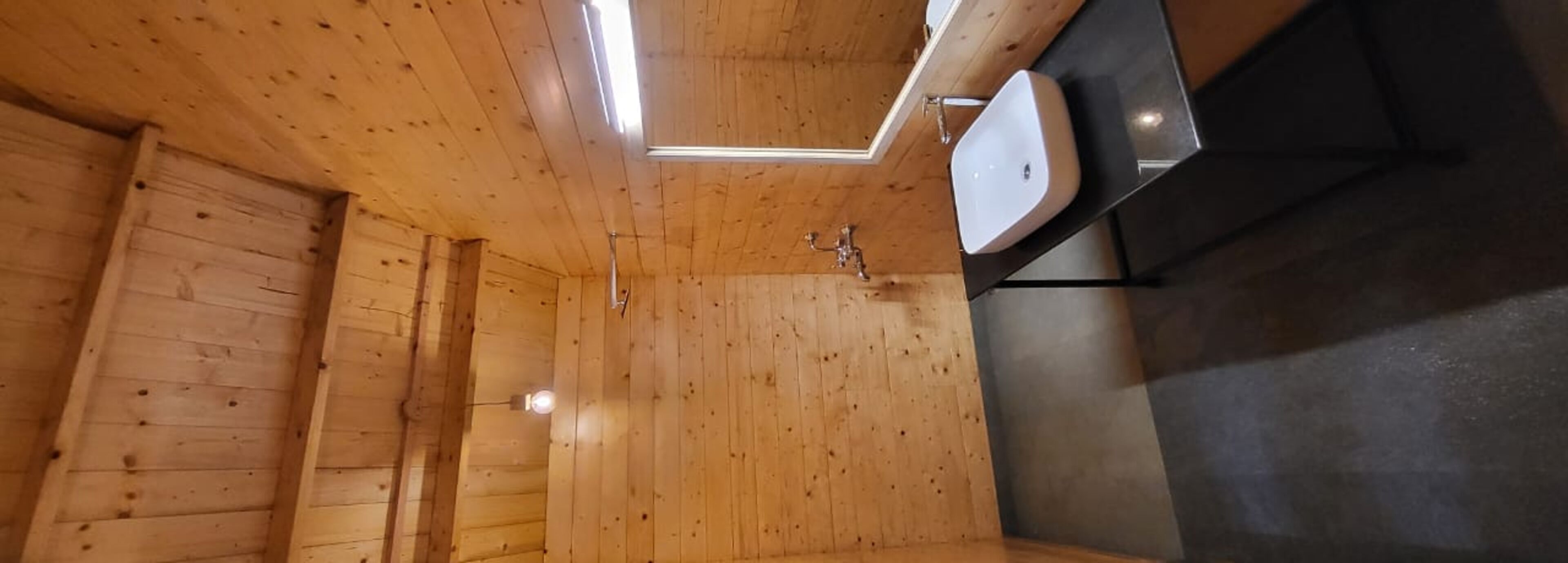 A wooden cabin interior with a wooden ceiling, a black countertop, and a white sink.