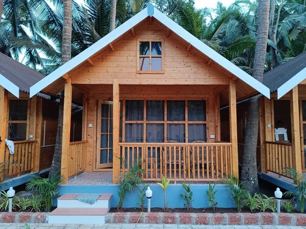 A wooden cabin with a pitched roof, large windows, and a porch with a railing. - Sand Tent Beach Resort Patnem (Canacona)
