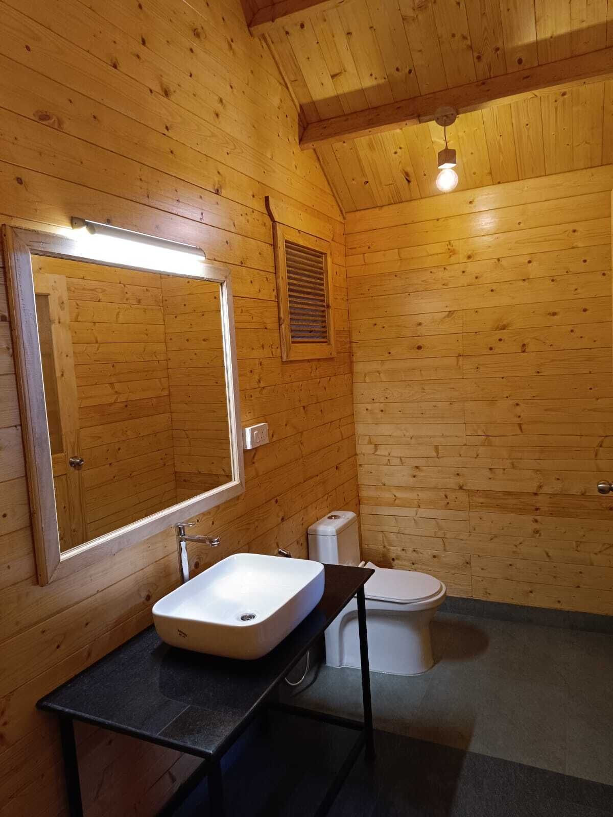 Een houten badkamer met een houten hutje, een rechthoekig wastafel, een toilet en een spiegel.