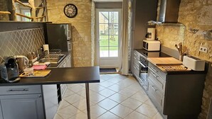 Une cuisine avec un plafond en bois, des murs en pierre, une horloge et une vue sur l’extérieur.