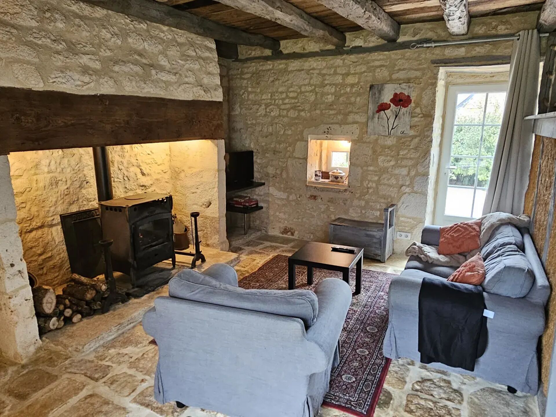 Habitació amb parets de pedra, una llar de foc, un sofà, una televisió i una finestra.