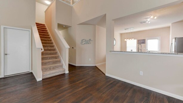 Un intérieur spacieux avec un escalier en bois, un coin cuisine doté d’un plan de travail et d’un évier, et un mur sur lequel est écrit le mot « Manger ».