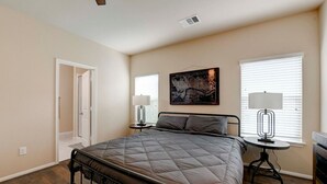 Une chambre à coucher avec un lit, des tables de chevet, une porte et un ventilateur de plafond.