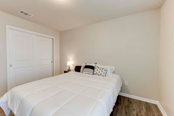 A bedroom with a large bed, a nightstand, a lamp, and a door.