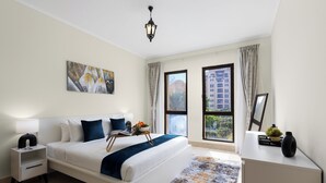 A modern hotel room with a large bed, bedside tables, a nightstand, a desk, a lamp, a window with curtains, and a view of buildings outside. - Maison Privee - Stylish & Spacious Apartment in Downtown Dubai (Dubai)