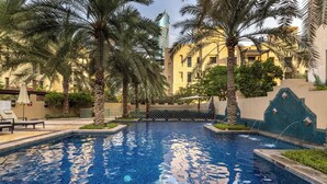 A swimming pool with palm trees, a high-rise building, and a tiled wall. - Maison Privee - Stylish & Spacious Apartment in Downtown Dubai (Dubai)
