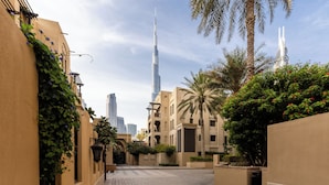 A paved pathway in a residential area with buildings, a tall skyscraper, and palm trees. - Maison Privee - Stylish & Spacious Apartment in Downtown Dubai (Dubai)