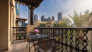 A balcony with a table and chair, a decorative fence, and a view of tall buildings. - Maison Privee - Stylish & Spacious Apartment in Downtown Dubai (Dubai)