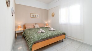 Une chambre à coucher bien rangée, avec un lit, deux tables de chevet, une horloge murale et une fenêtre avec des rideaux.