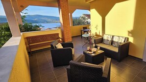 Un espace extérieur aménagé, abrité et doté de mobilier en osier, d’une petite table avec des boissons, et offrant une vue sur le paysage.