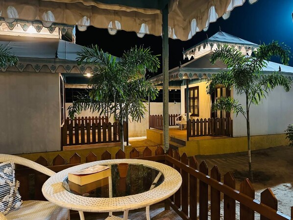 Un espace patio extérieur avec une table ronde et des chaises, entouré d’une clôture en bois et de plantes en pot.