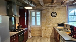 Une cuisine avec un mur en pierre, des poutres apparentes, une cuisinière à gaz et un four encastré.