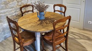 Une table ronde en bois, entourée de quatre chaises, un vase bleu contenant des plantes séchées, un tableau encadré accroché au mur et une porte blanche.