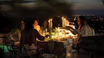 A group of people dining at an outdoor table with candles, surrounded by chairs and a pool.