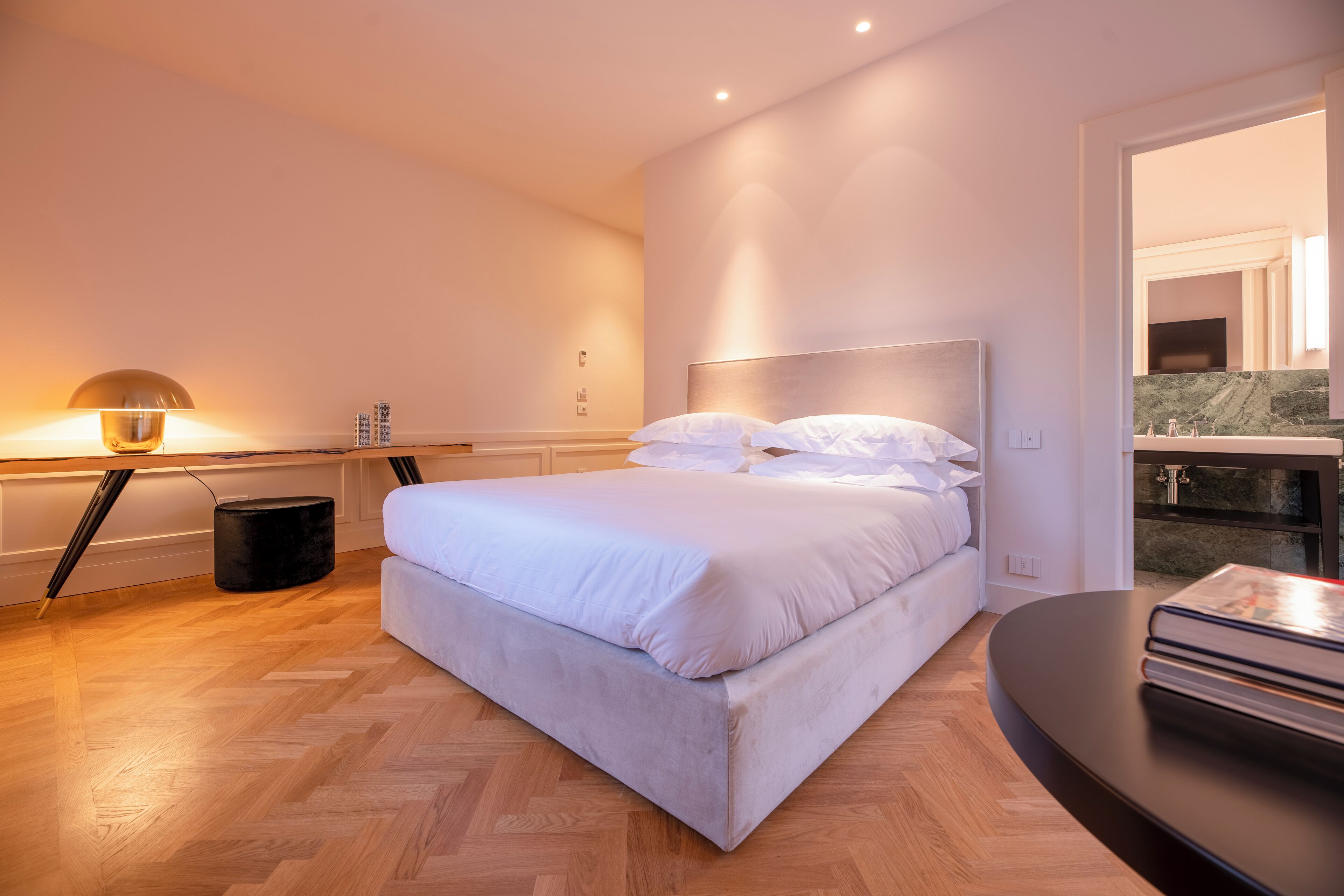 A modern bedroom with a large bed, a bedside table with a lamp, and a view of a balcony.
