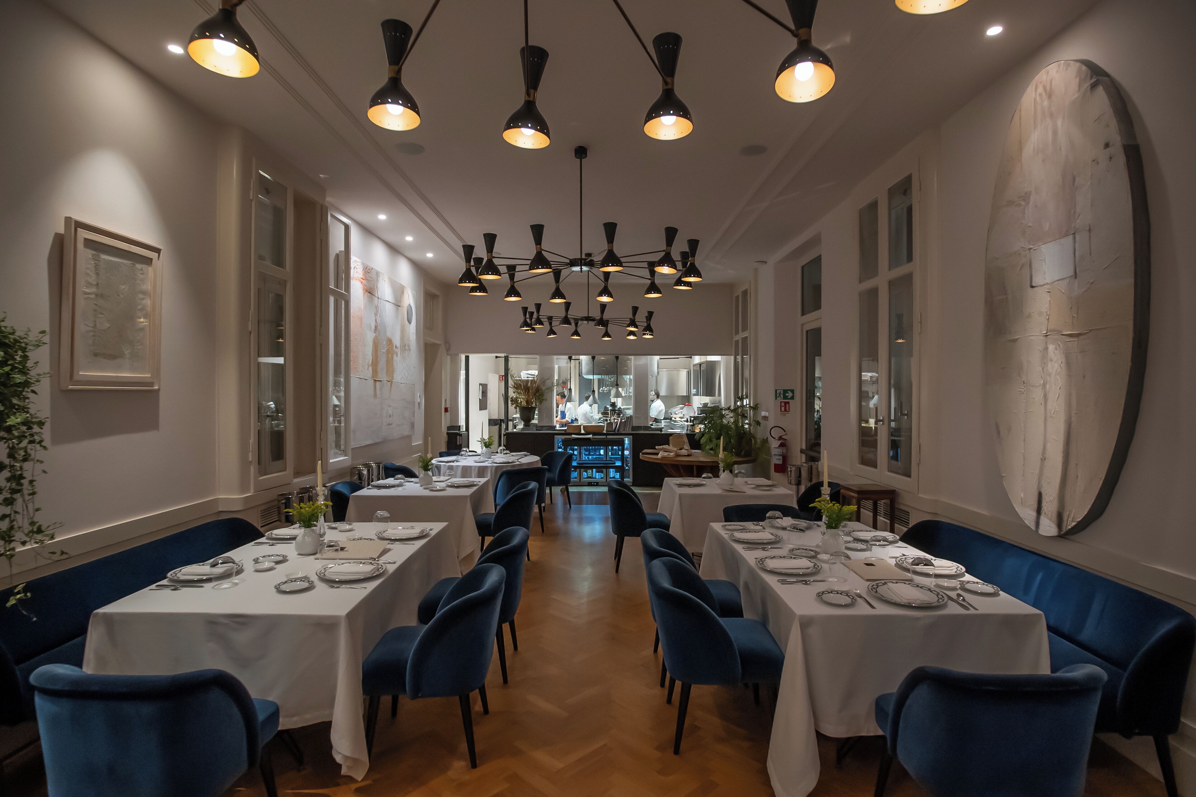 Un restaurante con varias mesas y sillas, una zona de bar al fondo e iluminación colgante.